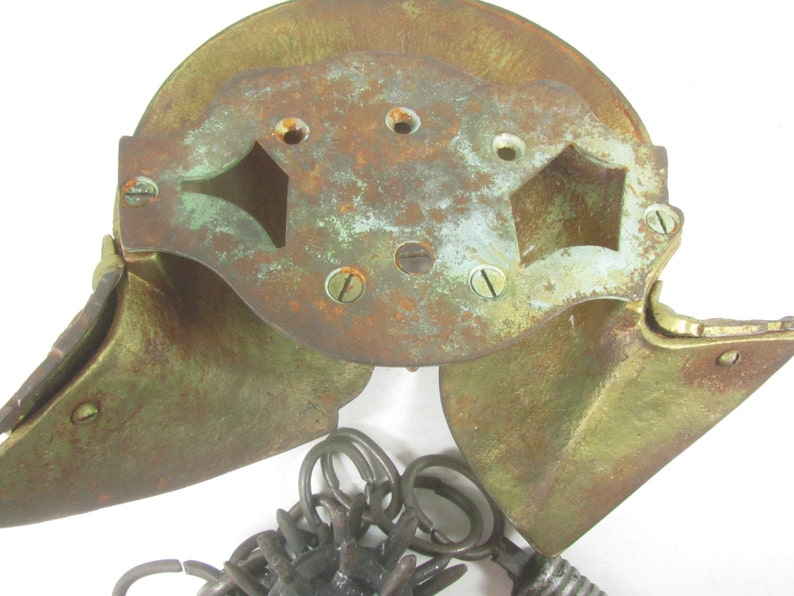 May include: A vintage brass door knocker with a decorative design. The knocker is in two pieces, with a hinged top and a bottom piece that swings open. The knocker is attached to a chain with a ring at the end.