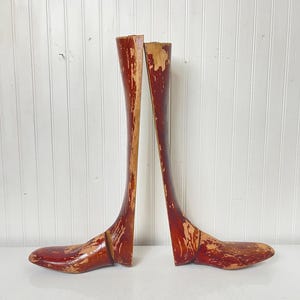 May include: A pair of wooden shoe trees with a reddish-brown finish. The shoe trees are made of wood and have a curved shape. They are designed to help maintain the shape of shoes.
