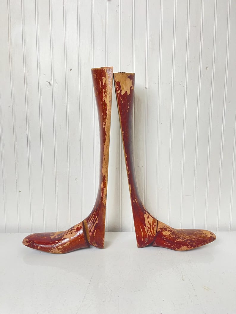 May include: A pair of wooden shoe trees with a reddish-brown finish. The shoe trees are made of wood and have a curved shape. They are designed to help maintain the shape of shoes.