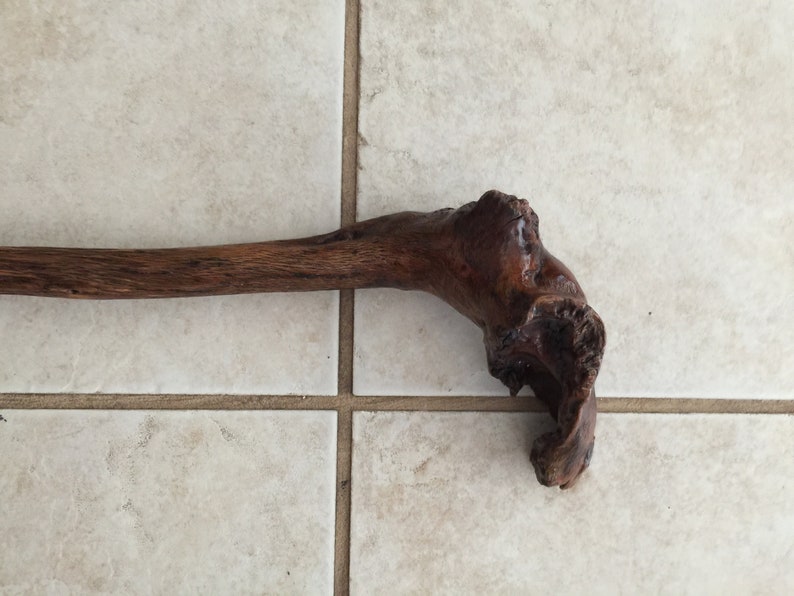 May include: A dark brown wooden walking stick with a unique, twisted handle.