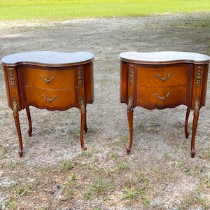 May include: A pair of antique wooden nightstands with ornate details and curved tops. Each nightstand has two drawers and sits on four legs.