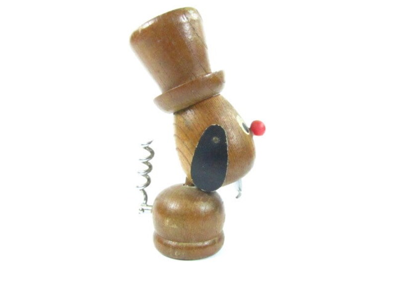 May include: A novelty wooden corkscrew shaped like a dog wearing a top hat. The dog has a black ear, a red nose, and a silver corkscrew. The corkscrew is made of wood and metal.