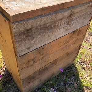 May include: A wooden storage box with a rustic, weathered finish. The box has a hinged lid and is made of natural wood planks.