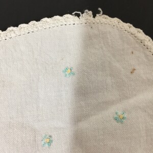 Op de afbeelding: Wit gehaakt tafellaken met een gegolfde rand en geborduurde blauwe bloemen met gele centra.