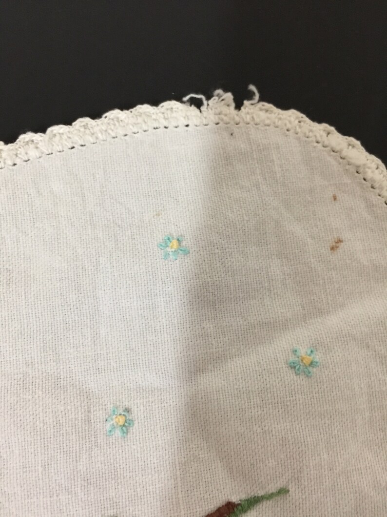 Op de afbeelding: Wit gehaakt tafellaken met een gegolfde rand en geborduurde blauwe bloemen met gele centra.