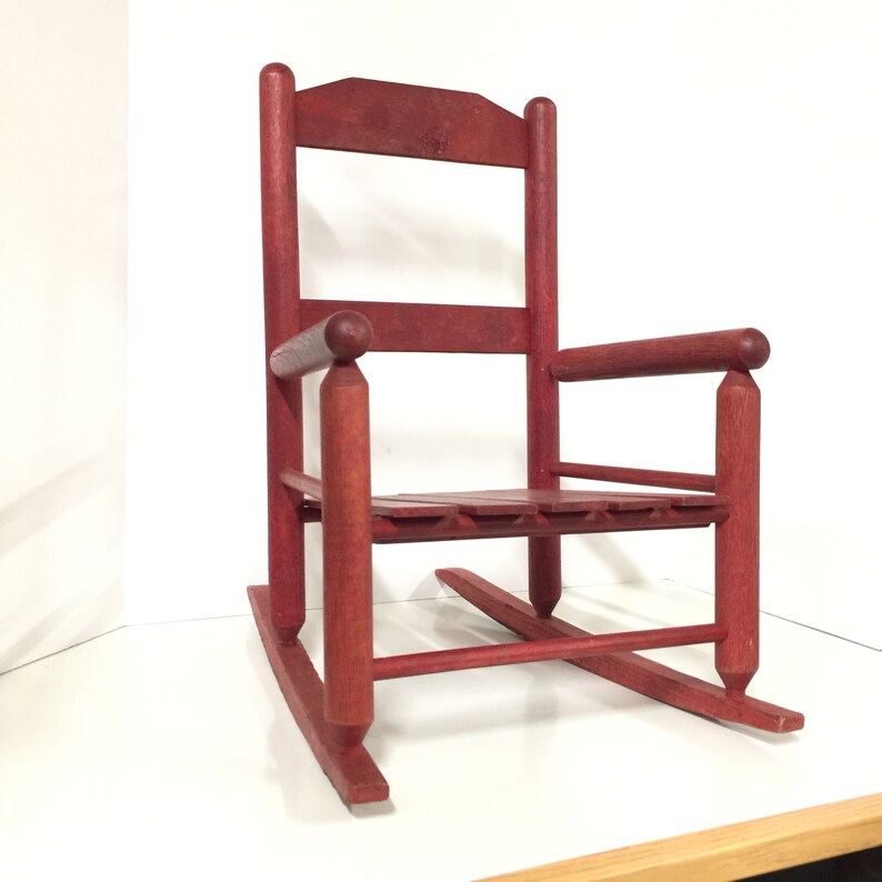 Puede incluir: Una silla mecedora de madera roja con un asiento de listones y un respaldo redondeado. La silla est&aacute; hecha de madera maciza y tiene un estilo r&uacute;stico, de granja.