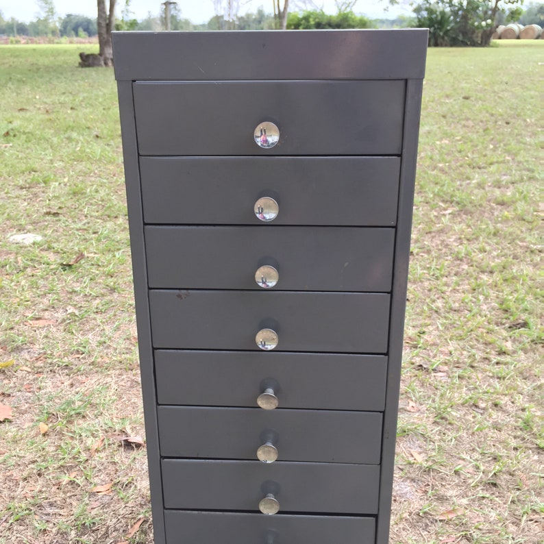 May include: A dark gray metal file cabinet with eight drawers and silver knobs.