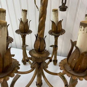 Pode incluir: Um candeeiro de metal dourado com seis l&acirc;mpadas e um centro de metal torcido. O candeeiro tem um design floral com uma borda festonada.