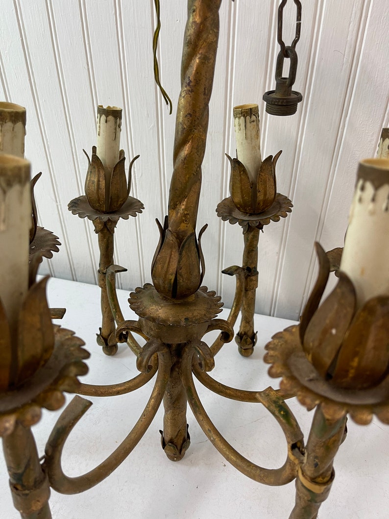 Pode incluir: Um candeeiro de metal dourado com seis l&acirc;mpadas e um centro de metal torcido. O candeeiro tem um design floral com uma borda festonada.