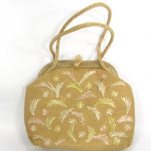 May include: A beige woven clutch bag with a floral embroidery design in pink and yellow thread. The bag has a top clasp closure and a rope handle.