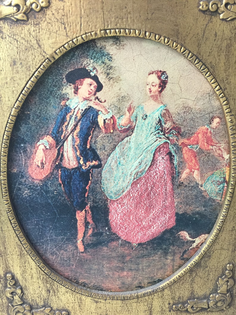 May include: An oval painting framed in gold, depicting a couple in a garden setting. The man is wearing a blue jacket and a black hat, while the woman is wearing a blue and red dress. The frame has ornate details.