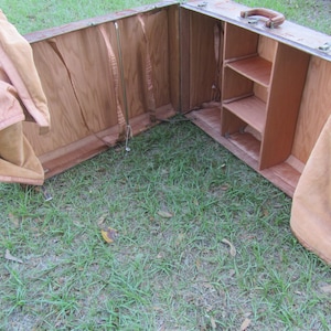 May include: An antique wooden travel trunk with a brown leather exterior and a fabric lining. The trunk is open and has a shelf inside.