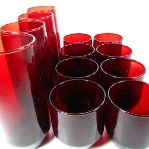 May include: A set of 12 red glass tumblers. The tumblers are arranged in a pyramid shape. The tumblers are all the same size and shape.