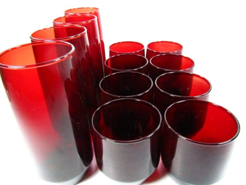 May include: A set of 12 red glass tumblers. The tumblers are arranged in a pyramid shape. The tumblers are all the same size and shape.