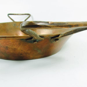 May include: A vintage copper pan with a hammered finish and a large, curved handle. The pan has a rustic, antique look.