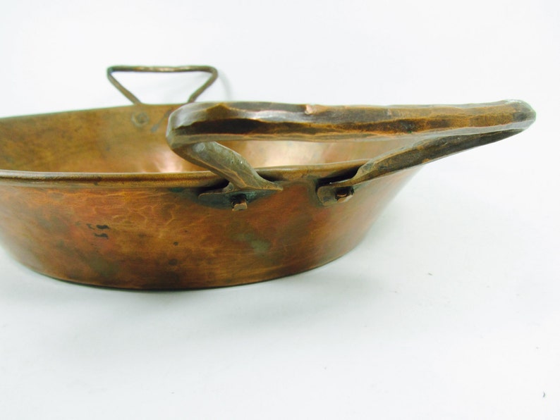 May include: A vintage copper pan with a hammered finish and a large, curved handle. The pan has a rustic, antique look.