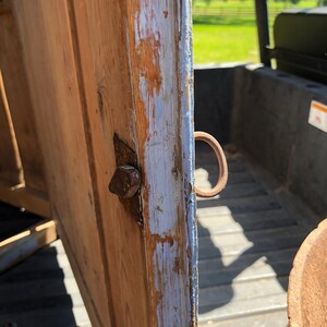 May include: Close-up of a wooden cabinet door with a metal hinge and a metal ring handle. The door is painted a light blue color and has some chipped paint. The wood is a light brown color.