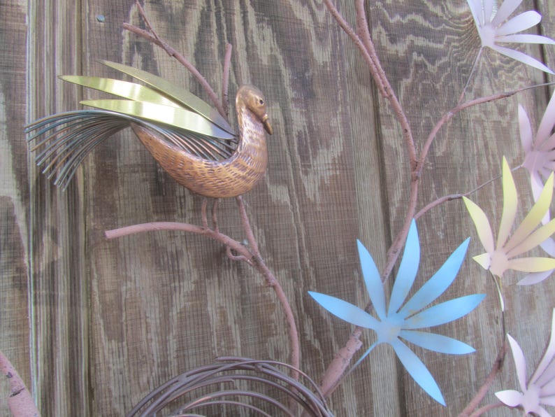 K&ouml;nnte beinhalten: Eine Wandskulptur mit einem stilisierten Vogel mit Kupfer- und Goldakzenten, der auf einem Ast mit Metallbl&auml;ttern in Blaut&ouml;nen, Gelb und Rosa sitzt.