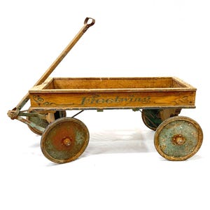 May include: An antique wooden wagon with the word "Fleetwing" painted on the side. The wagon has four wheels with a distressed, aged appearance. The handle is angled upwards, and the wagon bed is rectangular.