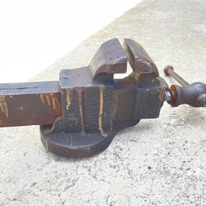 May include: A vintage cast iron vise with a black finish and a wooden handle. The vise is labeled "Columbian Vise & Mfg. Co. New York, N.Y. No. 12".