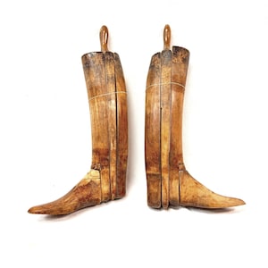 May include: A pair of vintage wooden boot trees with a light brown finish and visible wood grain. These adjustable shoe forms feature a segmented design with a vertical handle at the top, used to maintain the shape of tall boots.