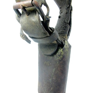 May include: A close-up of a vintage cowbell with a leather strap and buckle. The bell is made of metal and has a worn, rustic appearance.