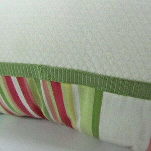 May include: A white pillow with a green trim and a striped fabric with pink, green, and white stripes.