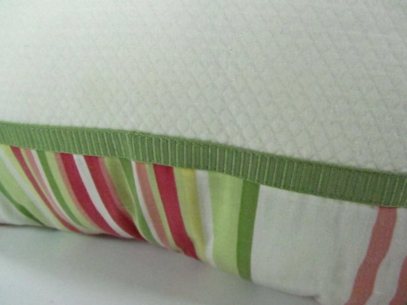 May include: A white pillow with a green trim and a striped fabric with pink, green, and white stripes.
