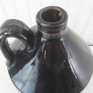May include: A black glazed ceramic jug with a wide mouth and a handle. The jug has a smooth, shiny finish.