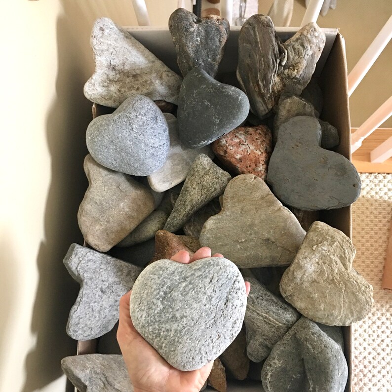 May include: A box filled with various heart-shaped stones in shades of gray, brown, and white. The stones are arranged in a random pattern, creating a visually appealing display.