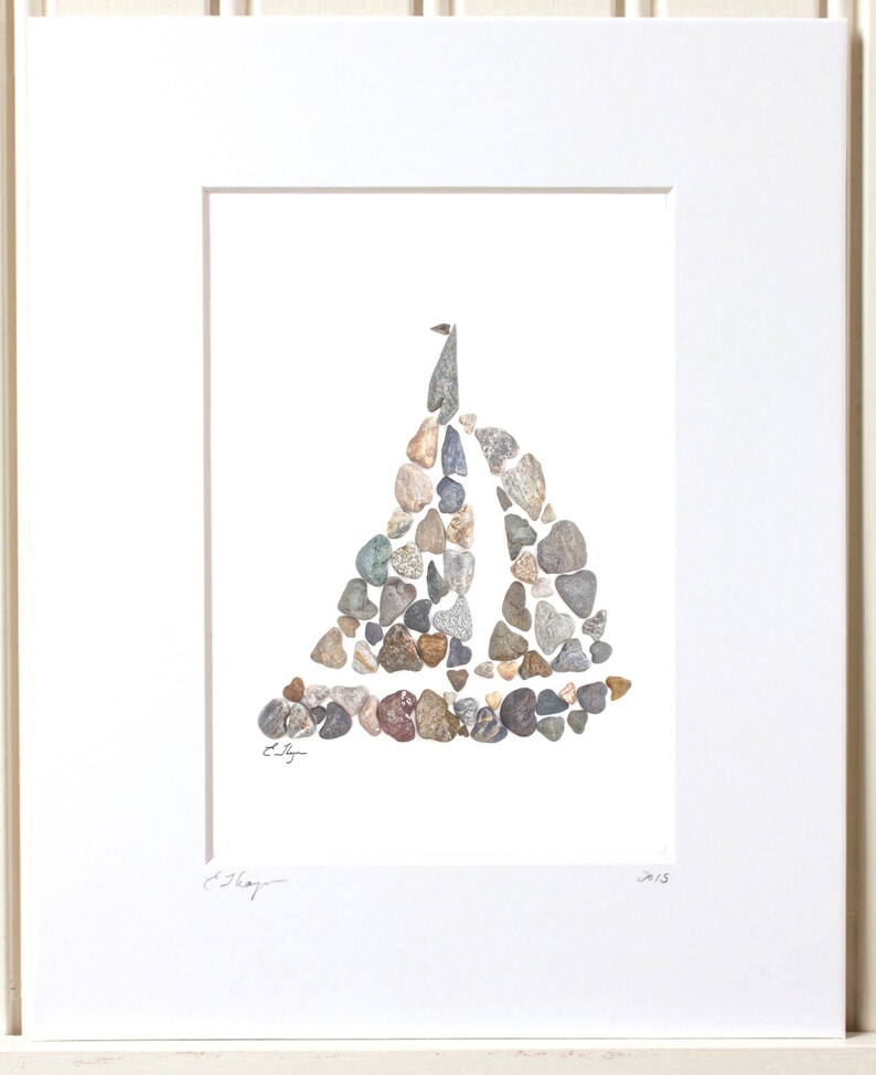 May include: A framed artwork featuring a sailboat made of small stones in shades of gray, brown, and beige. The artwork is signed "E. Shay" and dated "2013".