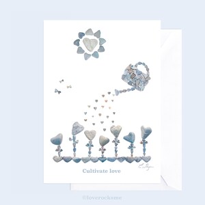 May include: A white card with a blue and gray pebble art design of a watering can pouring hearts into a row of heart-shaped flower pots. The text "Cultivate love" is printed below the design.