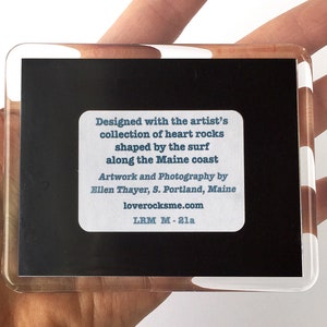 May include: A black and white photo of heart-shaped rocks, framed in a clear acrylic frame. The text on the back reads: "Designed with the artist's collection of heart rocks shaped by the surf along the Maine coast. Artwork and Photography by Ellen Thayer, S. Portland, Maine. loverocksme.com LRM M-21a"