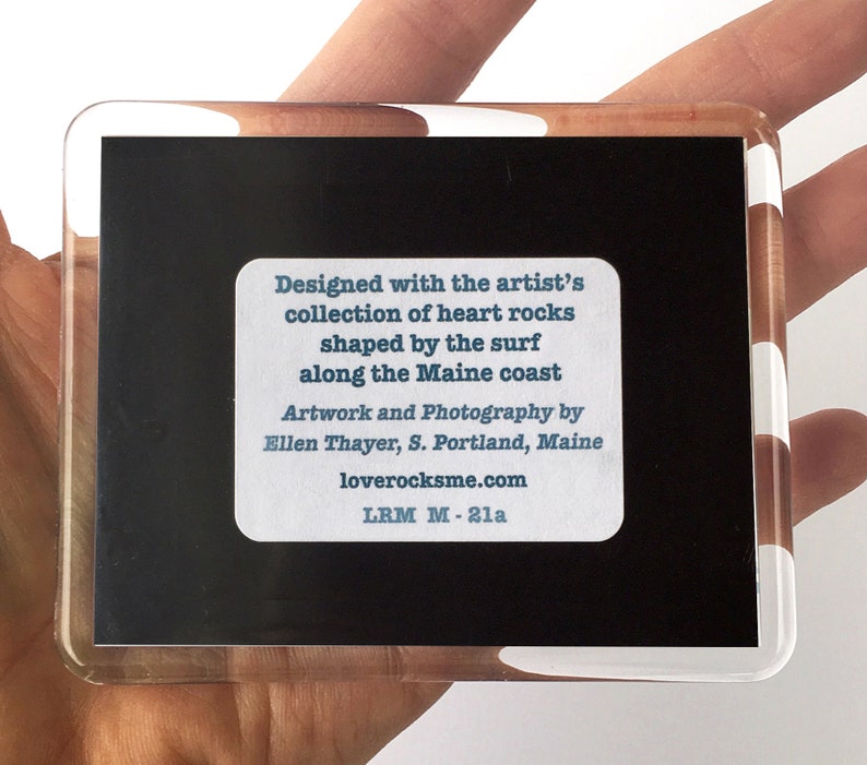 May include: A black and white photo of heart-shaped rocks, framed in a clear acrylic frame. The text on the back reads: "Designed with the artist's collection of heart rocks shaped by the surf along the Maine coast. Artwork and Photography by Ellen Thayer, S. Portland, Maine. loverocksme.com LRM M-21a"