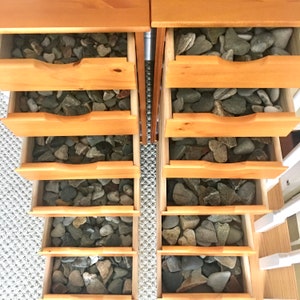 May include: Two wooden drawers with six drawers each, filled with smooth, gray, heart-shaped stones.