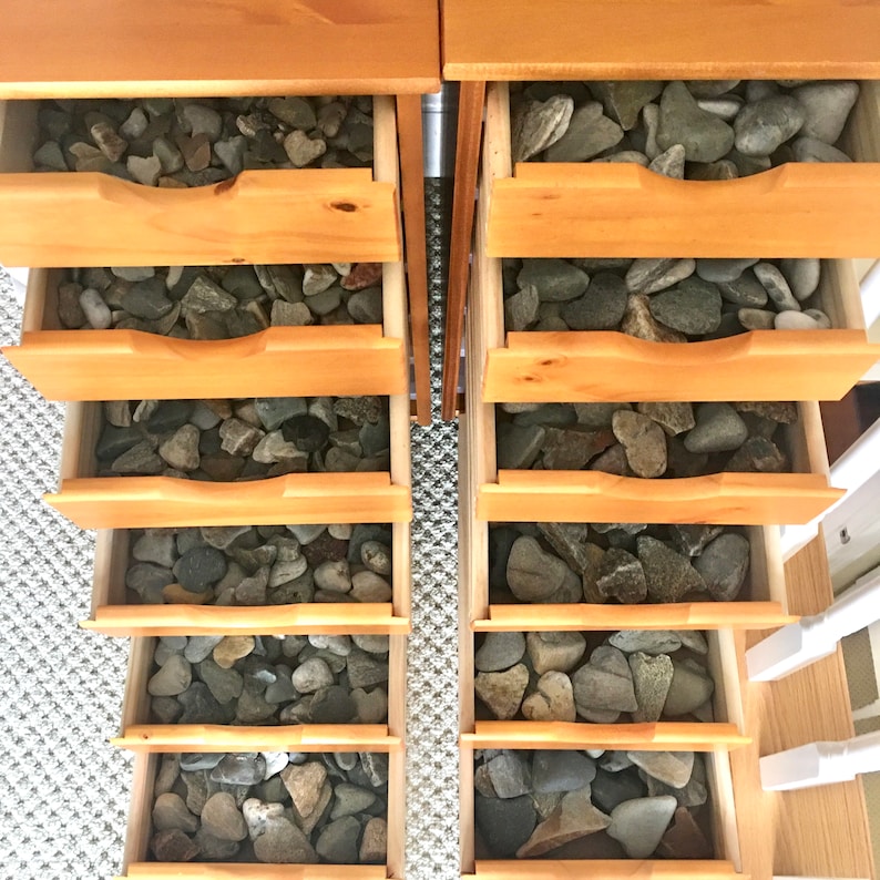 May include: Two wooden drawers with six drawers each, filled with smooth, gray, heart-shaped stones.