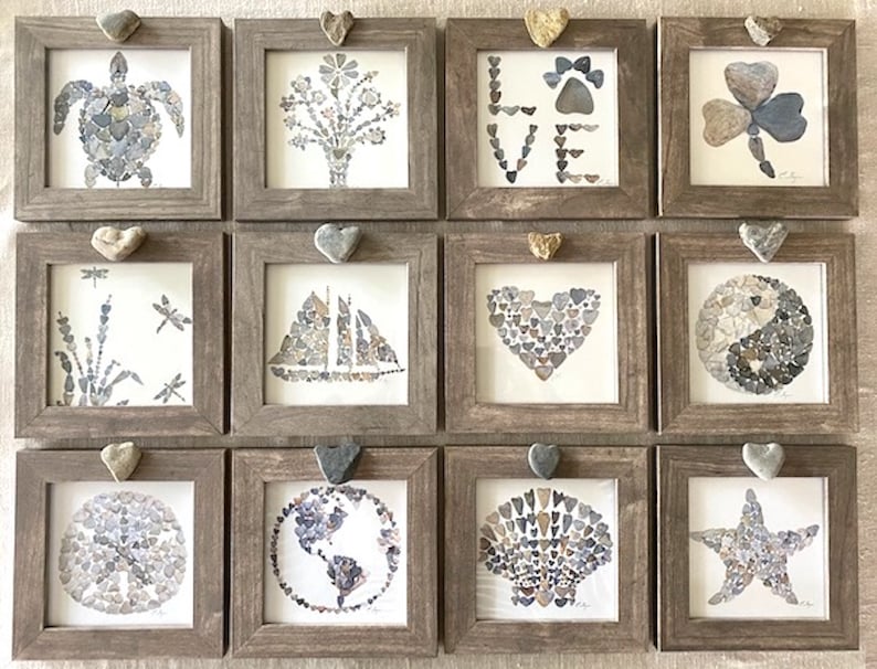 May include: Twelve framed square art pieces with a rustic brown frame and a heart-shaped hanger. Each piece features a different design made from small stones, including a turtle, a flower bouquet, the word "LOVE", a four-leaf clover, a dragonfly, a sailboat, a heart, a yin-yang symbol, a seashell, a globe, a starfish, and a circle.