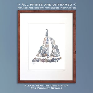 May include: A framed print of a sailboat made from small stones. The sailboat is white with a blue sail and is set against a white background. The print is framed in a dark wood frame.