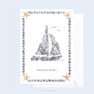 May include: A greeting card with a sailboat made of small stones. The sailboat is surrounded by a border of small hearts. The card reads "Deck the Hulls!"