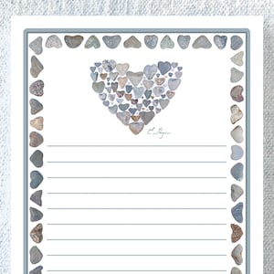 May include: A white card with a blue border features a heart shape made of small, heart-shaped stones. The stones are various shades of brown, gray, and white. The card has lined writing space and the signature "E. Slayton" at the bottom.