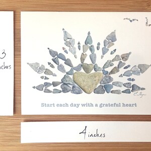 May include: A white card with a gray stone heart surrounded by smaller gray stones in the shape of a sunburst. The text "Start each day with a grateful heart" is printed below the stones. The card measures 4 inches by 3 inches.