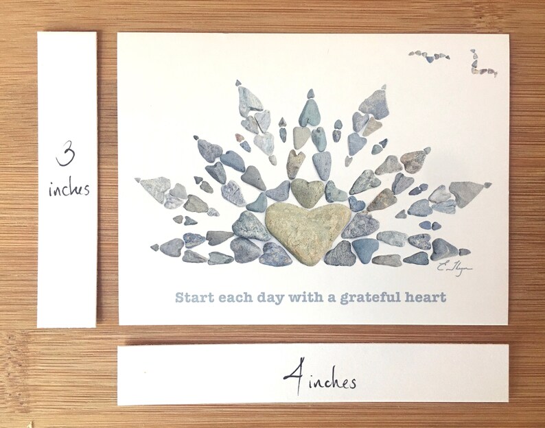 May include: A white card with a gray stone heart surrounded by smaller gray stones in the shape of a sunburst. The text "Start each day with a grateful heart" is printed below the stones. The card measures 4 inches by 3 inches.