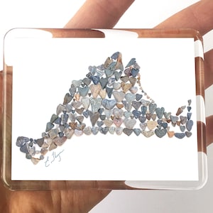 May include: A white background with a framed image of the outline of Long Island, New York, created with small, heart-shaped stones. The stones are various shades of gray, brown, and white. The image is signed "E. Meyer" in the lower left corner.