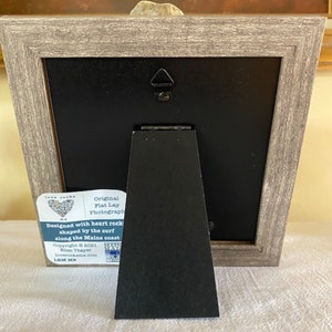 May include: A framed photograph of a heart-shaped rock with the text "Original Flat Lay Photograph" and "Designed with heart rock shaped by the surf along the Maine coast" on a white label attached to the frame.