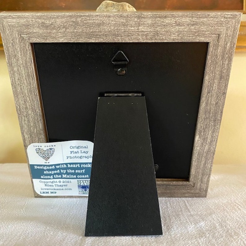 May include: A framed photograph of a heart-shaped rock with the text "Original Flat Lay Photograph" and "Designed with heart rock shaped by the surf along the Maine coast" on a white label attached to the frame.