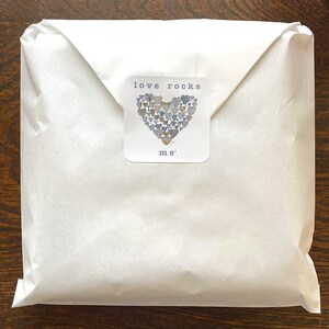 May include: White paper packaging with a sticker that says "love rocks me" and features a heart made of small rocks.