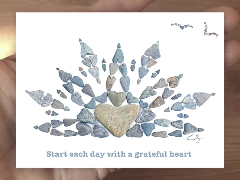 May include: A white card with a blue stone heart surrounded by smaller blue stones in the shape of a sunburst. The text "Start each day with a grateful heart" is printed below the image.