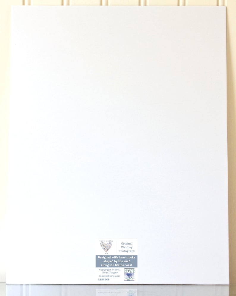 May include: A white canvas print with a heart-shaped design made of heart-shaped rocks. The text "Original Flat Lay Photograph" is printed below the heart. The text "Designed with heart rocks shaped by the surf along the Maine coast" is printed below the photograph. The text "Copyright &copy; 2001 Ellen Thayer loverockame.com LUM MP" is printed below the design. The text "Maine Heart Rocks" is printed in a blue box below the copyright information.
