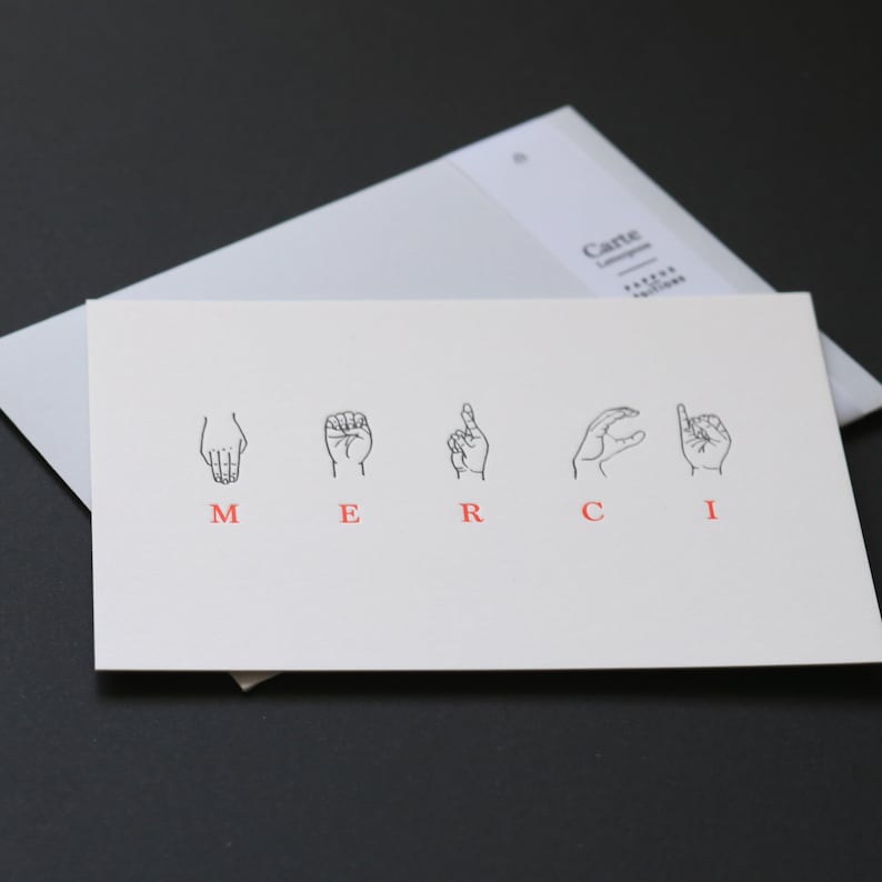 May include: A white card with the word "MERCI" spelled out in red letters. Each letter is represented by a hand sign in American Sign Language.
