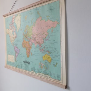 K&ouml;nnte beinhalten: Eine Vintage-Weltkarte in einem Holzrahmen. Die Karte ist auf einem hellblauen Hintergrund mit braunen, orangen und rosafarbenen Kontinenten gedruckt. Die Karte tr&auml;gt den Titel "Planisphere" und enth&auml;lt die W&ouml;rter "Ocean Atlantique", "Ocean Pacifique" und "Ocean Indien".